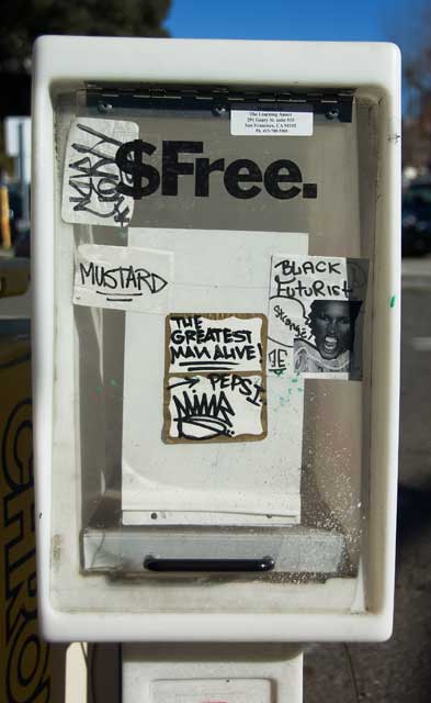 Graffiti on a sidewalk free paper box on Grand Avenue in Oakland.
